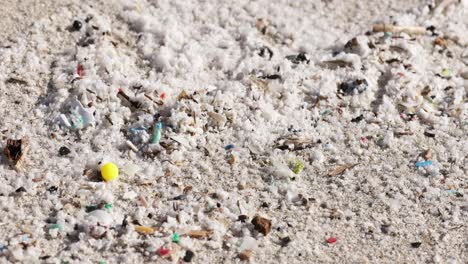 Close-up-of-microplastics-and-debris-scattered-on-sandy-beach-in-daylight