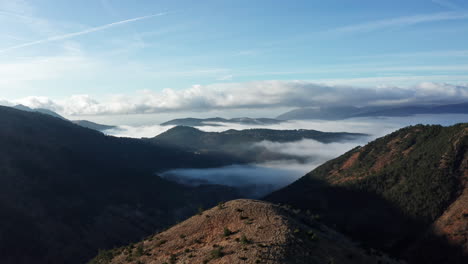 Morgenlicht-Taucht-Die-Bergige-Landschaft-In-Nebel-Gehüllte-Täler-Und-Einen-Klaren-Blauen-Himmel-über-Uns,-Eine-Heitere-Luftaufnahme