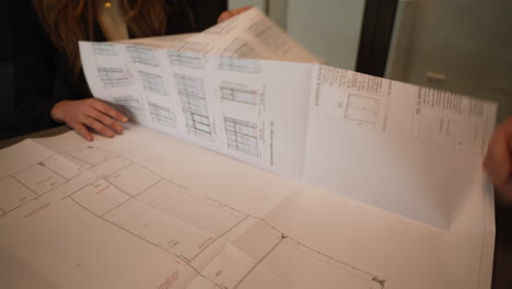 Smart-dressed-architect-discuss-blueprint-plans-in-consultation-with-young-adult-female-client