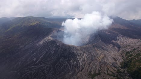 Soaring-above-the-clouds,-unveils-the-stunning-volcanic-activity-of-Mount-Bromo,-Billowing-smoke-and-fiery-eruptions-create-a-breathtaking-scene,-aerial-4k-drone-footage
