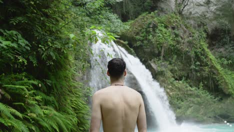 Muscular-young-white-man-stands-in-front-of-Kawasan-Falls-raising-arms-to-take-in-epic-views