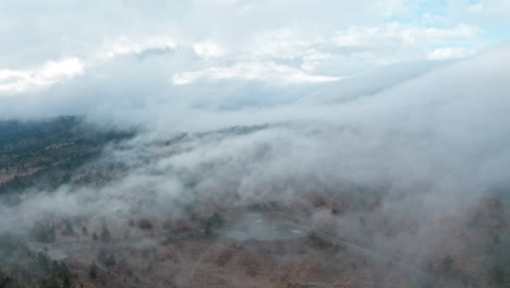 Eine-Neblige-Landschaft-Mit-Wolken,-Die-Im-Morgengrauen-über-Die-Hügel-Rollen,-Luftaufnahme