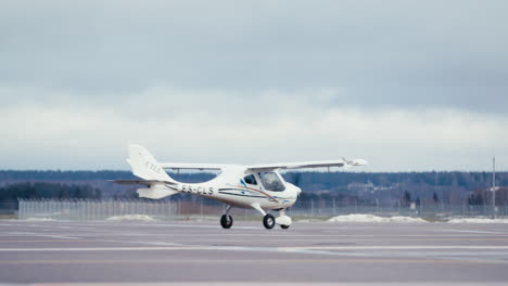 Ultralight-aircraft-taxiing-through-static-shot-on-airfield-apron-tarmac-with-snow-visible-in-background