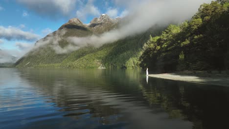 Mystery-woman-in-elegant-dress-standing-on-shore-of-alpine-lake-in-sunshine