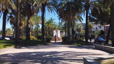 Junge-Fährt-Kickbike-Scooter-Im-Park-Mit-Brunnen-In-Antibes,-Frankreich