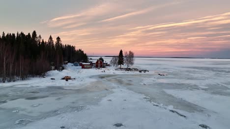 Frozen-bay-at-dusk-with-red-houses,-Bothnian-Bay-near-Lulea,-Sweden,-serene