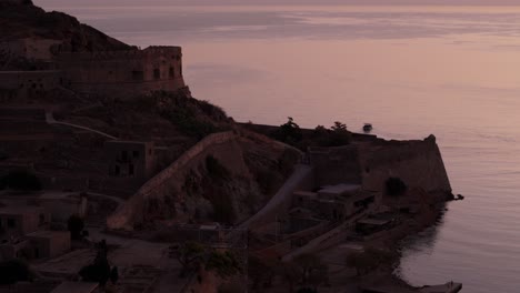 Orange-last-light-glow-on-ocean-reflects-off-historic-fortress-ruins-as-boat-leaves-island