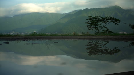 El-Impresionante-Lago-Kawaguchiko-En-Honshu,-Japón,-Muestra-Exuberantes-Montañas-Verdes-Al-Fondo,-Reflejando-Edificios-En-Sus-Tranquilas-Aguas,-Personificando-La-Serenidad-Del-Lago.