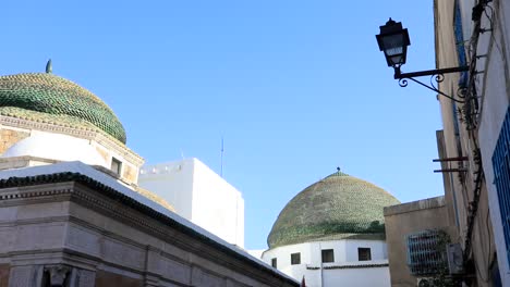 Blue-sky-over-Turbe-el-Bey-mausoleum-in-Tunis,-sunlight-on-historic-domes,-street-lamp-in-view