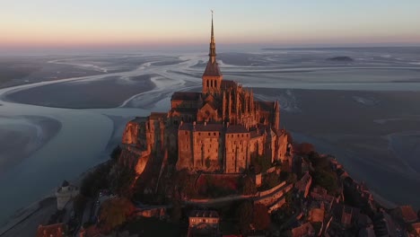 Drone-flying-toward-and-over-Mont-Saint-Michel-at-sunset,-Normandy-in-France