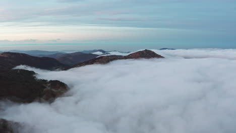 Misty-mountains-at-dawn-with-a-thick-blanket-of-clouds-rolling-through-valleys,-serene-and-majestic