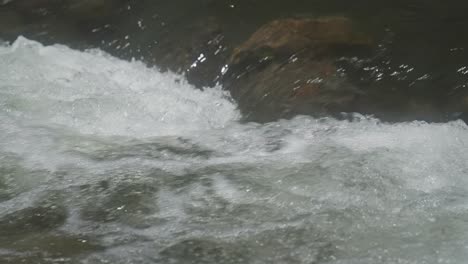 Close-up-of-water-rapids-flowing-over-underwater-boulders,-slowmo
