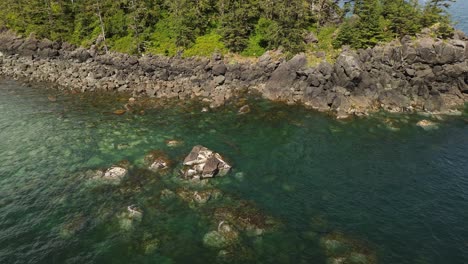 Toma-Aérea-De-Un-Dron-Flotando-Sobre-El-Borde-Del-Agua-Con-Una-Costa-Rocosa-Cerca-De-Un-Arenero,-Grey-Bay,-Canadá