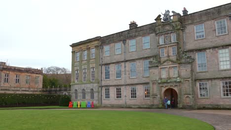 Historic-Lyme-House-in-Cheshire-with-green-lawn-under-overcast-sky,-colorful-signs-in-foreground