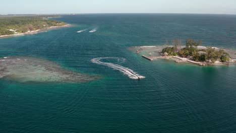 Speed-boat-drives-quickly-across-channel-outside-of-Utila-Honduras,-aerial-overview