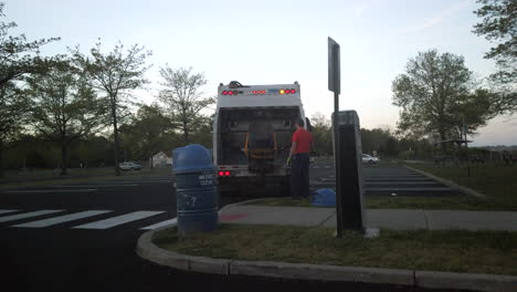 Trabajador-Sanitario-Vaciando-Un-Cubo-De-Basura-En-Un-Camión-En-Un-Parque-Al-Atardecer