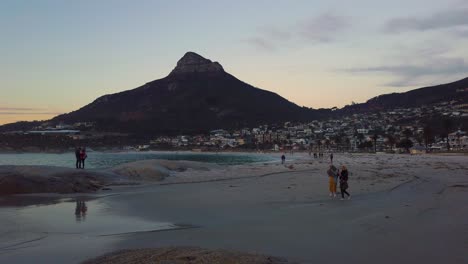 Tourists-on-beach-at-Camp's-Bay-at-dusk-with-Lion's-Head-in-background