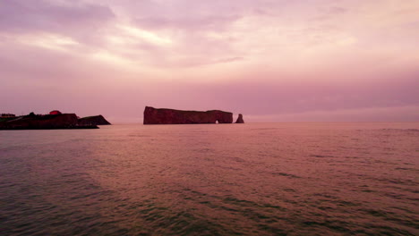 Drone-view-receding-from-Percé-Rock-in-Gaspésie-during-a-cloudy-sunset
