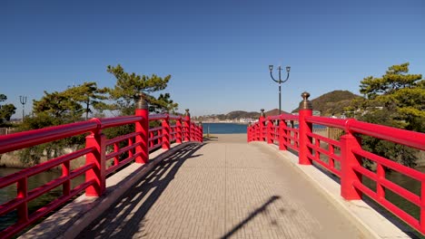 Typische-Rote-Japanische-Holzbrücke,-Die-An-Einem-Sonnigen-Tag-Mit-Blauem-Himmel-Zum-Meer-Führt