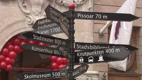 Close-up-of-a-multi-directional-signpost-with-distances-to-landmarks,-red-balloons-in-background