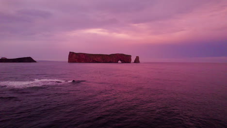 Drone-view-receding-from-Percé-Rock-during-a-cloudy-sunset-above-the-Saint-Lawrence-River