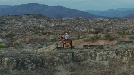 Cowboy-on-Horseback-in-Tatacoa-Desert-Ridge-Landscape,-Cinematic-Aerial-Reveal