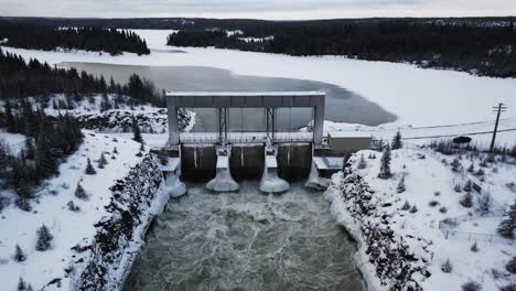 Drone-out-Long-Snow-Covered-Road-with-Aerial-Slow-Drone-Orbit-Rushing-Water-Notigi-Hydroelectric-Dam-in-the-Arctic