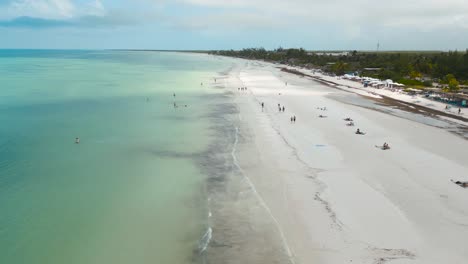 Wide-angle-aerial-drone-view-of-the-busy-sandy-white-beaches-of-the-tropical-island-of-Holbox-in-Mexico-during-a-really-hot-sunny-day-shot-in-4k
