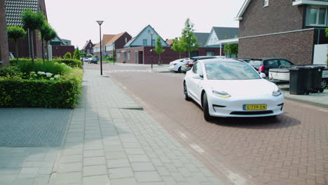Sleek-modern-design-of-white-Tesla-turning-right-onto-home-driveway-on-sunny-day