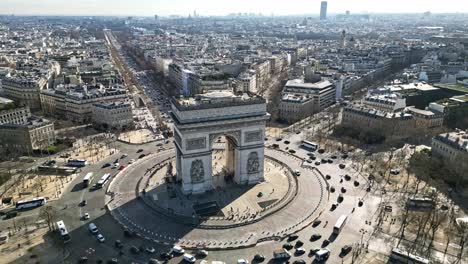 Triumphal-arch-or-Arc-de-Triomphe-and-car-traffic-on-roundabout-with-Paris-cityscape,-France