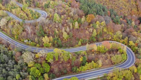 Aerial-flyover-mountain-road-in-autumn-forest,-vehicles-on-country-thoroughfare