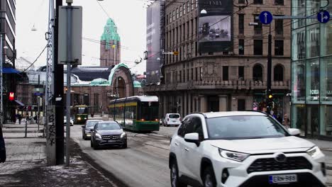 Overcast-day-in-Helsinki-with-tram-and-cars,-city-life-in-motion,-iconic-architecture-of-Helsinki-Central-station-in-background