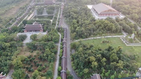 Drohnen-Luftaufnahme-In-Vietnam,-Die-Bei-Sonnenuntergang-über-Buddhistische-Tempelanlagen-Mit-Pagoden-Und-Mit-Grünen-Bäumen-Bedeckten-Straßen-In-Ninh-Binh-Fliegt