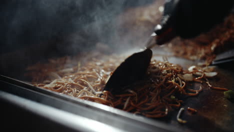 Stirring-around-noodle-dish-on-festival-grill-using-metal-spatulas