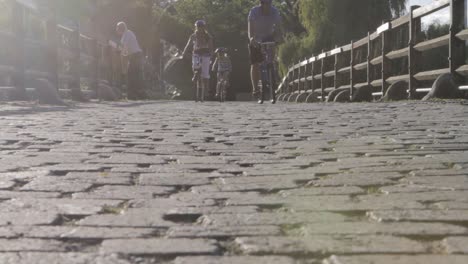 Low-angle-shot-of-people-cycling-on-a-cobblestone-path-with-pedestrians,-warm-sunlight,-outdoors