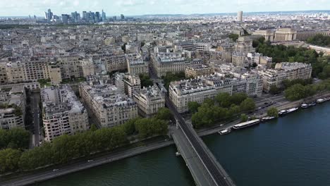 Flying-over-bridge-crossing-Seine-river-with-skyscrapers-of-La-Defense-district-skyline-in-background,-Paris