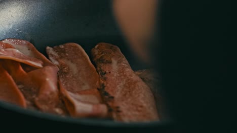 Close-up-shot-captures-person-using-fork-to-flip-sizzling-bacon-in-frying-pan