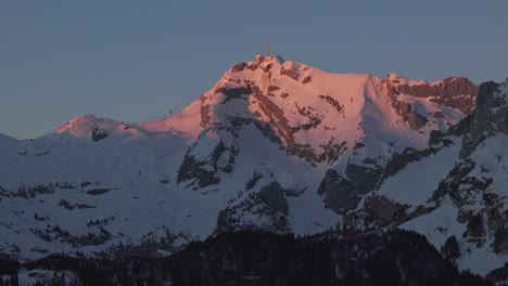 Aerial-view-showcasing-the-tranquil-ambiance-of-sunrise-over-a-majestic-snowy-mountain-range-silhouette,-filmed-by-drone