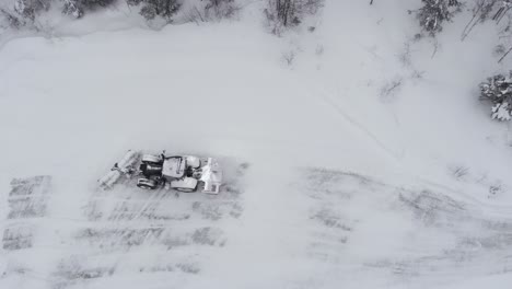 A-Tractor-Navigating-a-Snow-covered-Country-Road-Bordered-by-Dense-Coniferous-Trees---Aerial-Drone-Shot
