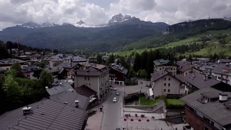 Low-aerial-through-Alpine-Village-towards-mountains,-Dolomites-Italy