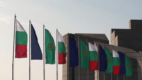 Tourist-walking-by-row-of-flags-outside-Bulgarian-State-Monument,-Shumen