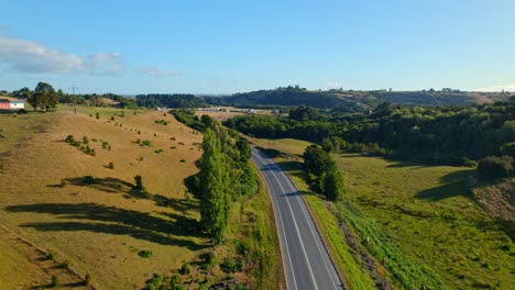 Vista-De-Pájaro-De-Un-Coche-Que-Pasa-Por-Un-Camino-Rural-Con-Prados-Al-Atardecer,-Chiloé,-Chile