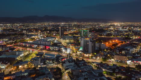 El-Tiempo-Aéreo-Del-Atardecer-Recorre-La-Ciudad,-Las-Luces,-El-Tráfico-Y-El-Edificio.