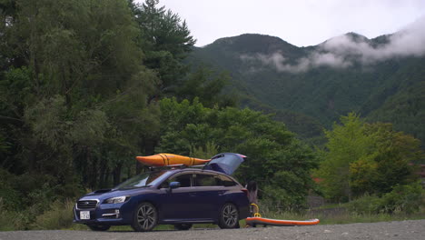 Un-Coche-Familiar-Azul-Está-Aparcado,-Donde-Se-Ve-A-Una-Niña-Arreglando-Su-Kayak,-Lista-Para-Pasar-Un-Agradable-Día-Por-Delante.