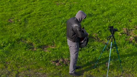 Photographer-Man-Setting-Up-A-Camera-Tripod-In-The-Grass-Field---Wide-Shot