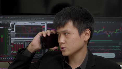Chinesischer-Geschäftsmann-Telefoniert-Mit-Der-Börse-Auf-Computermonitoren-Im-Hintergrund