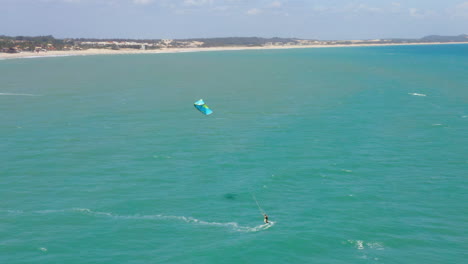 Vista-Aérea-De-Una-Persona-Practicando-Kitesurf-Y-Un-Pequeño-Pueblo-Alrededor,-Cumbuco,-Ceará,-Brasil