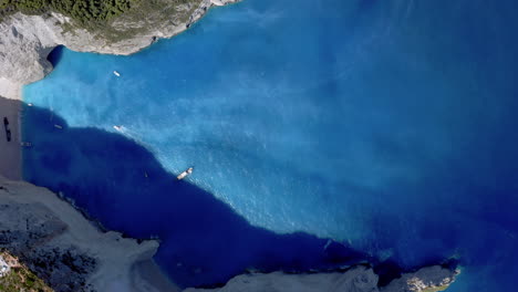 Aerial:-Top-down-shot-of-Navagio-beach-in-Zakynthos,-Greece-while-the-beach-is-in-shade