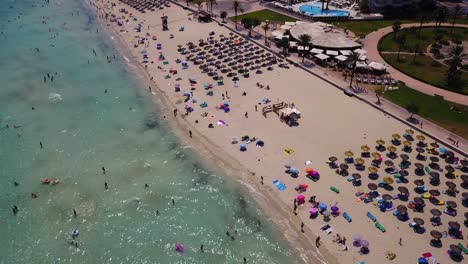 Cala-major-beach-with-colorful-umbrellas-and-tourists-swimming,-aerial-view