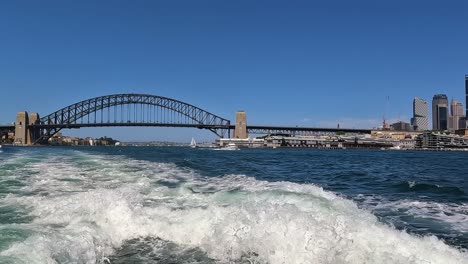 Pan-across-Sydney-harbour-bridge-from-view-of-transport-ferry-boat-in-water